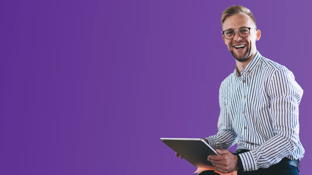 A smiling man in a striped shirt sits with a digital tablet in front of a purple background