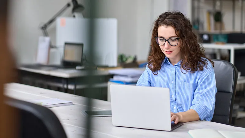 A woman works in front of a laptop in a bright office setting