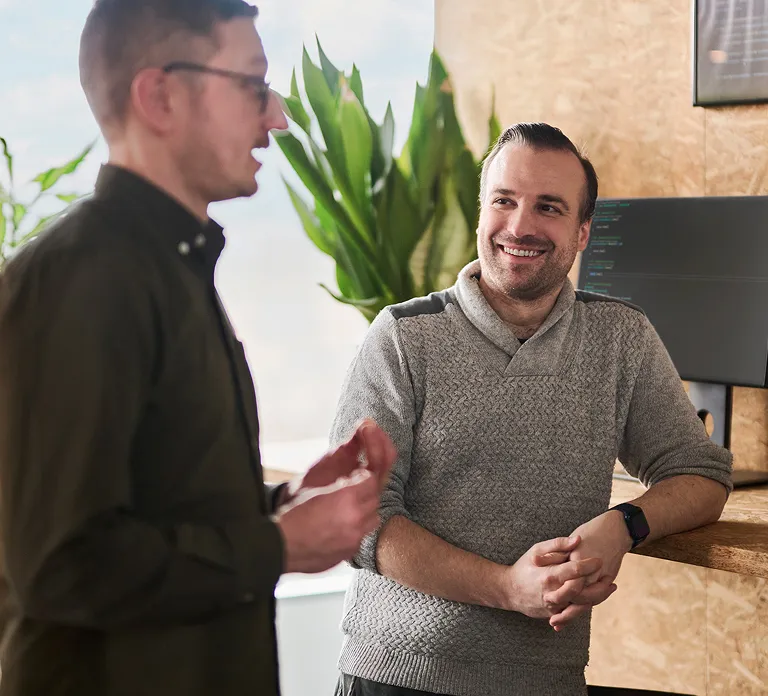 Two men engaged in conversation while standing in front of a computer screen.
