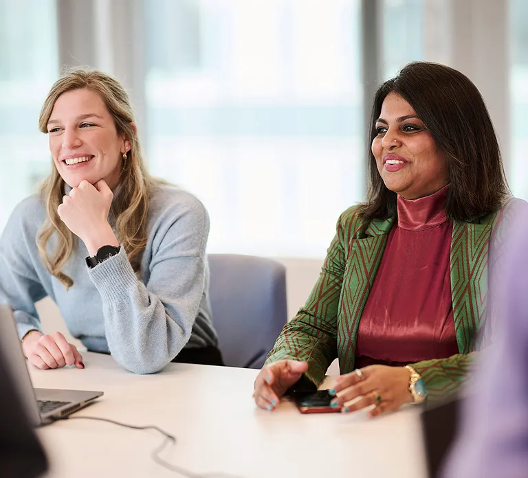 Two women engaged in discussion at a conference table in a modern office setting.
