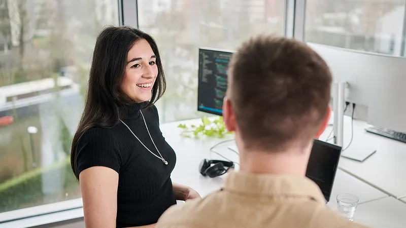 A woman converses with a man in a modern office setting, both engaged in discussion.