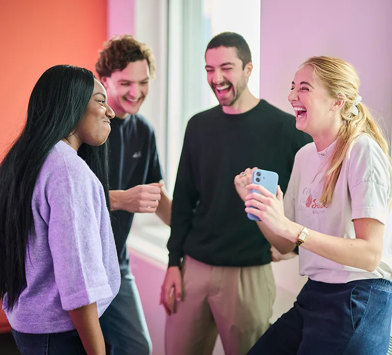 Four individuals are joyfully laughing and smiling as they hold a mobile phone, sharing a lighthearted experience.