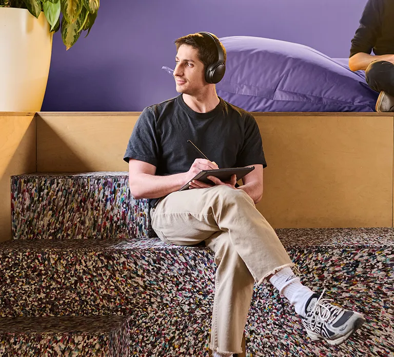 A man sitting, wearing headphones, appears focused and relaxed while enjoying music or a podcast.