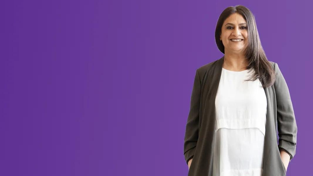 A woman has her hands in her cardigan pockets in front of a purple background