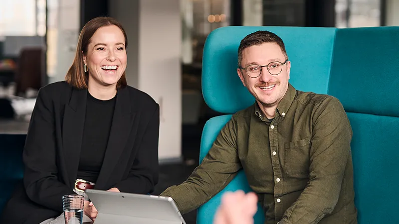 Two happy people collaborating while sitting in a chair, engaged with a laptop.
