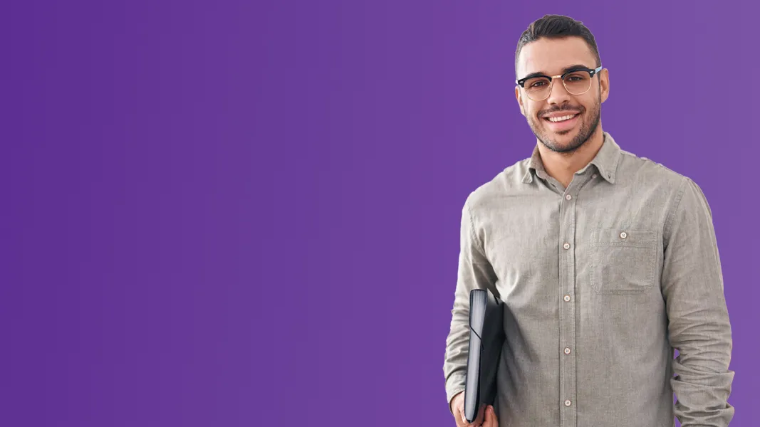 A man holds a laptop tucked under his arm in front of a purple background