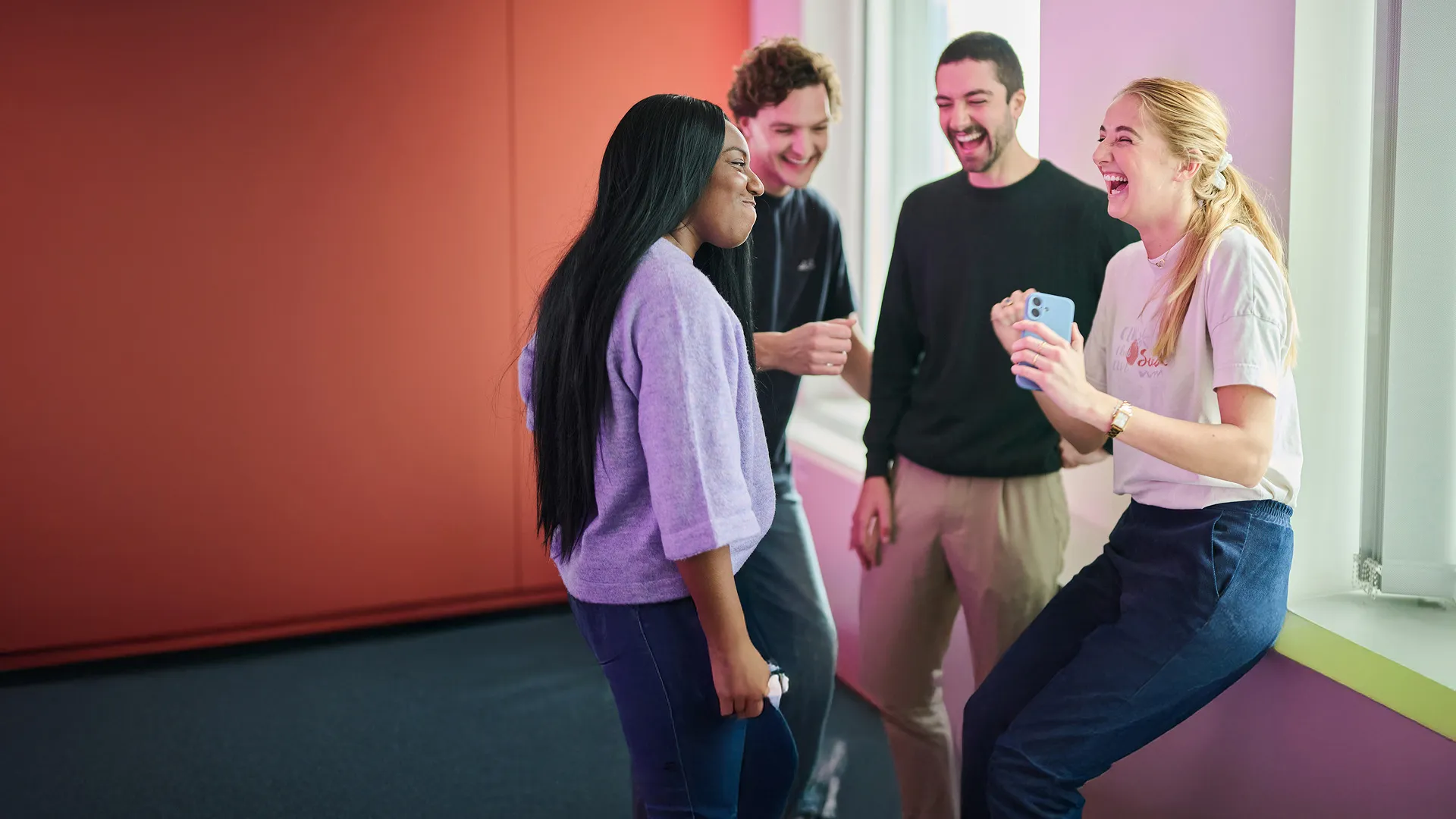 Four individuals are joyfully laughing and smiling as they hold a mobile phone, sharing a lighthearted experience.
